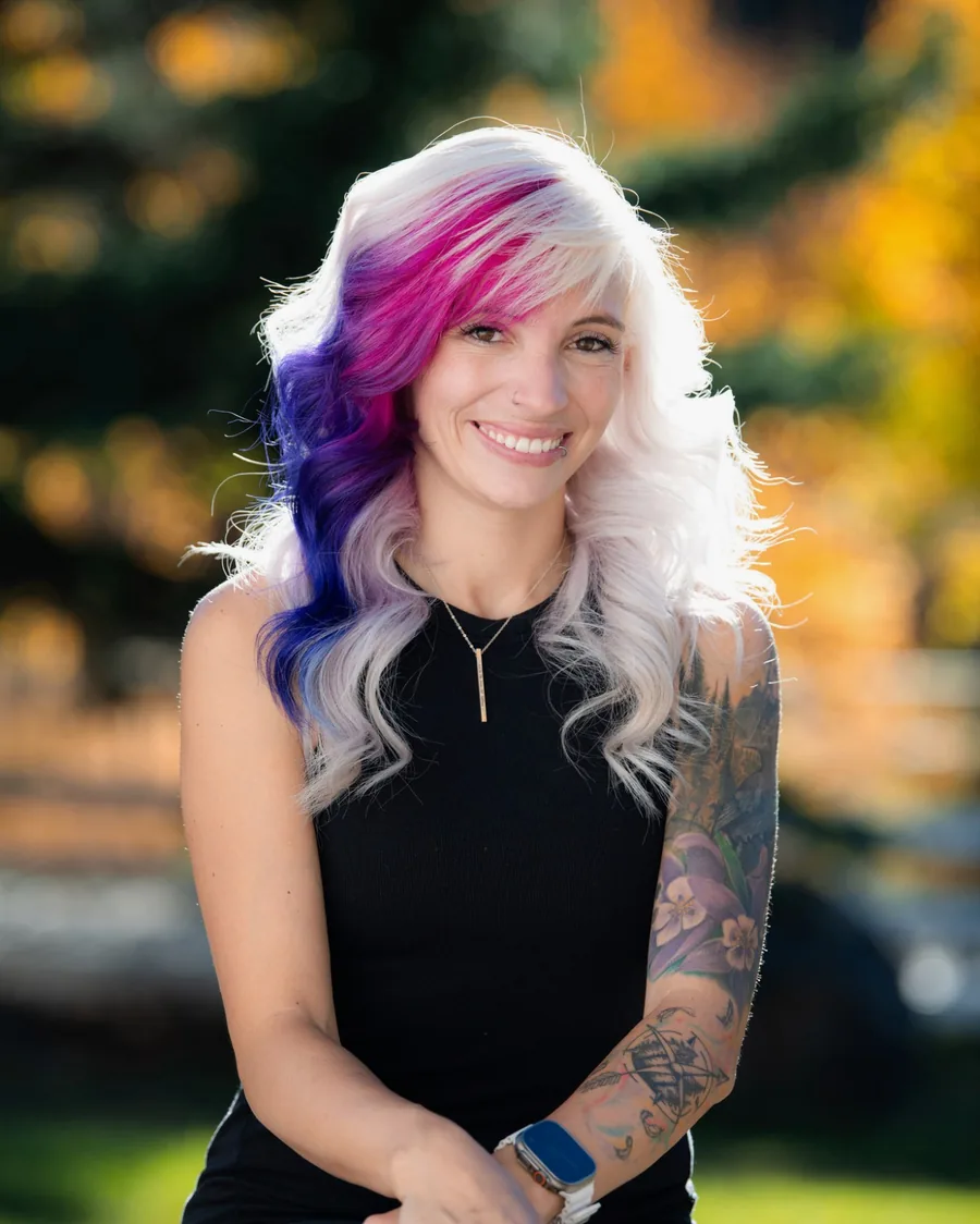 Kelly Adams, owner of Lash & Length, smiling outdoors with long platinum, pink and violet waves